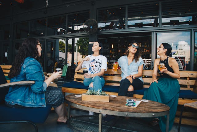 Vrouw met drie vriendinnen op een terras. Ze drinken, lachen uitbundig en stralen plezier en zelfvertrouwen uit.