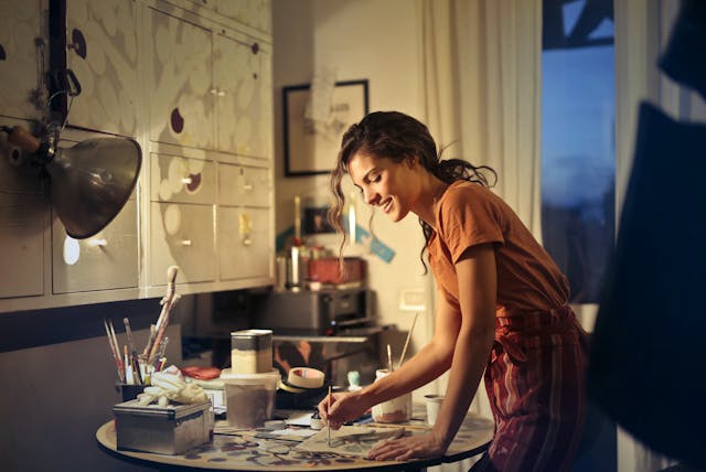 Lachende vrouw schildert. Ze geniet zichtbaar van haar nieuwe hobby, precies het beeld dat bij haar ex een gevoel van FOMO kan oproepen.