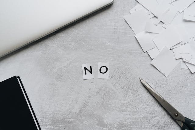Zwart-witfoto van een tafel met losse papiertjes waarop het woord ‘NO’ is gevormd, een subtiele weergave van de kracht van zelfrespect en grenzen stellen.