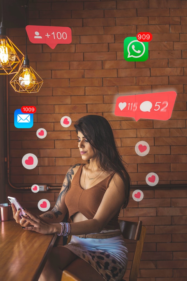 Vrouw kijkt naar haar telefoon, omringd door hartjes en meldingen. Ze zoekt bevestiging en aandacht via social media, net als veel ex-partners na een breuk.