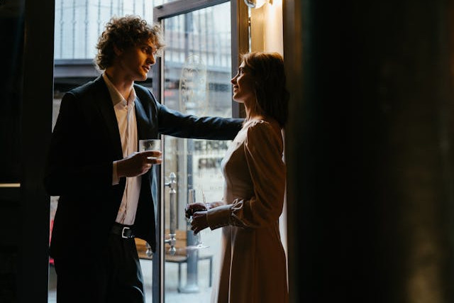 Man en vrouw in gesprek in de deuropening met een glas in de hand. 