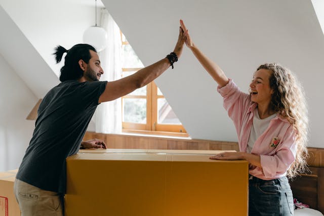 Man en vrouw geven elkaar een high five boven een verhuisdoos. Ze werken samen aan een nieuwe start in hun relatie.