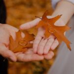 Twee handen die elkaar raken, elk met een herfstblad en een trouwring als symbool voor een huwelijk dat op het punt staat te breken of te herstellen.