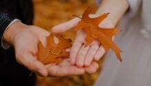 Twee handen die elkaar raken, elk met een herfstblad en een trouwring als symbool voor een huwelijk dat op het punt staat te breken of te herstellen.