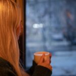 Vrouw kijkt uit het raam naar een besneeuwd landschap met een kop koffie in haar hand nadat haar ex heeft gezegd dat het nooit meer goedkomt.