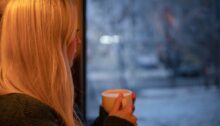 Vrouw kijkt uit het raam naar een besneeuwd landschap met een kop koffie in haar hand nadat haar ex heeft gezegd dat het nooit meer goedkomt.