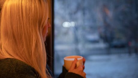 Vrouw kijkt uit het raam naar een besneeuwd landschap met een kop koffie in haar hand nadat haar ex heeft gezegd dat het nooit meer goedkomt.